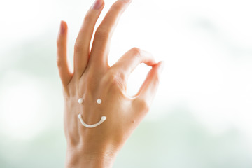 Closeup woman beautiful hands with long fingers applying moisturising and soothing cream on skin. Funny smiling faces, emoji. Ok Sign. 