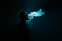 The Young Man Smoke A Cigarette Against The Background Of The Bright Light