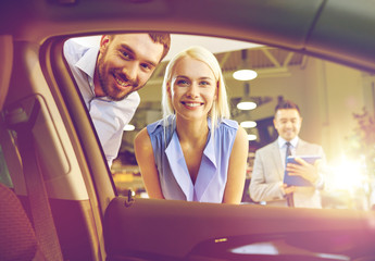 happy couple with car dealer in auto show or salon