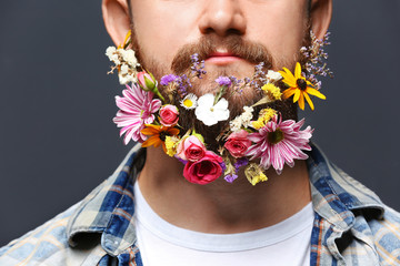 Handsome man with beard of flowers on dark background