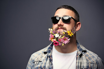 Handsome man in sunglasses with beard of flowers on dark background