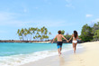 © Maridav - Happy couple from behind holding hands running having fun on tropical beach vacation. Hero view of people walking together in the splashing waves happy on summer holidays.