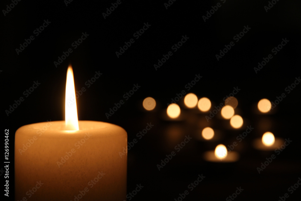 weiße Kerze brennt vor Teelichtern im Dunkeln Stock Photo