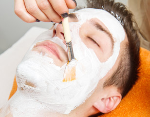 Therapist applying a face mask to a beautiful young man in a spa