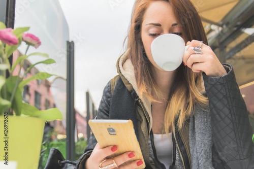 Fotografie, Obraz Attractive girl using smartphone at restaurant drinking coffe