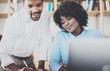 © SFIO CRACHO - Group of young coworkers working together in a modern office.African black business partners using laptop and discussing new startup project.Horizontal,blurred.