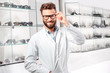 Portrait of a handsome ophthalmologist in front of the showcase with eyeglasses in the hospital