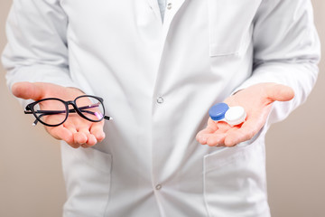 Eye doctor choosing between eyeglasses and lenses standing in front of the eye chart in the cabinet