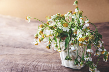 white flowers in basket on wooden table with brown paper background, vintage tone.