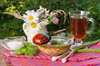 Миска с окрошкой, зелень, соус, бокал с квасом и букет садовых цветов на салфетке на столе
