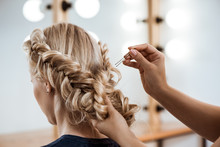 Female Hairdresser Making Hairstyle To Blonde Girl In Beauty Salon.