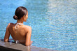 Luxury travel wellness resort bikini woman relaxing in swimming pool. Hydrotherapy spa retreat from behind on side of infinity pool looking away at blue water copyspace. Relaxation vacation concept.