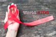 Red ribbon awareness on human hand with aged wood background with text message World aids day December 1: Symbolic concept for raising awareness/ concerns/ help and campaign on people with HIV concept