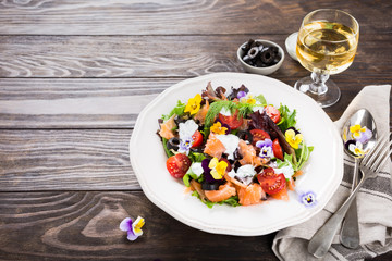 Wall Mural - Fresh salad with smoked salmon, black olives, cherry tomatoes and edible flowers on wooden background.