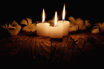 Candle light with frangipani flowers on wooden desk in black background soft focus(selective focus).