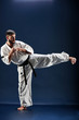 © amixstudio - Karate man in a kimono hits foot on a blue background