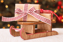 Wrapped Gift On Wooden Sled And Christmas Tree With Lights In Background