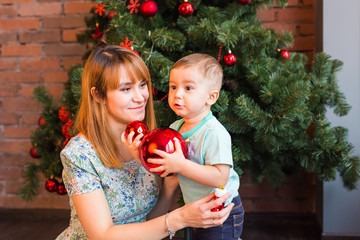 Mother helping little boy to decorate christmas tree at home