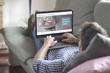 © GENETTICA - Young man lying on the sofa while using laptop with healthcare videoblog on the screen. View from behind. All screen graphics are made up.
