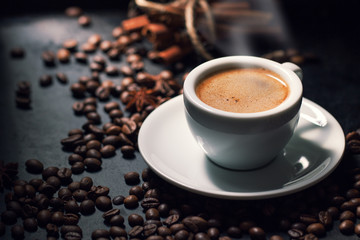 Fresh tasty espresso cup of hot coffee with coffee beans on dark