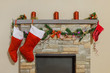 Mantelpiece decorated with Christmas candles, socks, pine tree branches, garland and ribbons above fireplace.