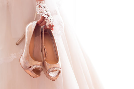 Beautiful bride in white wedding dress is holding shoes in her hands. Beauty model girl in bridal gown for marriage.