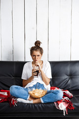 Girl eating chips, drinking soda, watching tv, sitting at sofa.