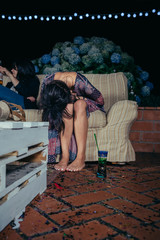 Young drunk woman holding her head sitting in the sofa in a outdoors party. Fun and alcohol and drugs problems concept.