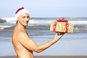 Man wearing the christmas hat standing on the beach with the present