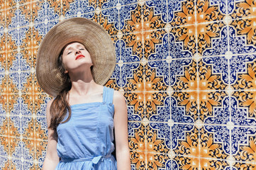 Portrait of beautiful elegant lady wearing hat against a traditional tiles azulejo wall.