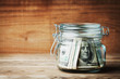 Dollar bills in glass jar on rustic table. Saving money concept.
