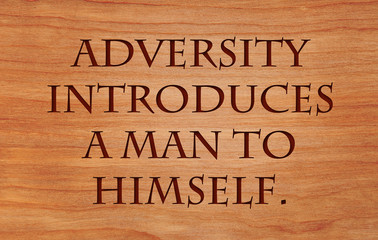 Adversity introduces a man to himself - quote on wooden red oak background