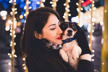 Beautiful young brunette woman with Jack Russell terrier enjoying Christmas or New Year night on a city street.