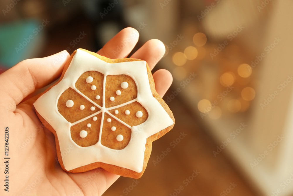 Female hand holding tasty gingerbread cookie on blurred background, close up view