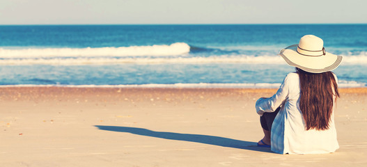 Wall Mural - Woman in a hat sitting on the beach