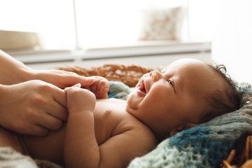 baby smiling at mother, close-up. adorable newborn child looking up at mother and holding her hands.