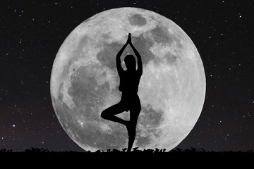 silhouette young woman with good shape practicing yoga under full moon at night with stars