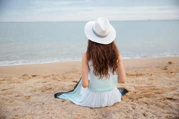 Wall Mural - Back view of young woman sitting on the beach