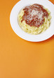 A dinner dish of spaghetti Bolognese on a bright orange background with blank space below