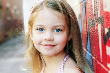 Smiling happy child leaning up against a graffiti wall in the city looking directly into the camera. 