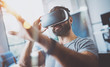 Closeup of bearded young man wearing virtual reality goggles in modern coworking studio. Smartphone using with VR headset. Horizontal, blurred.