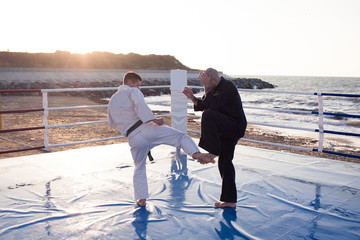 Two professional male karate fighters are fighting on the beach boxing ring