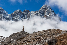 Mountain Cairn On Everest Base Camp Route In Himalayas, Nepal. Beautiful Cloudy Landscape With Cairn On The Big Rock And Arrow Pointing Down The Trail With Mountain Peak On Background.