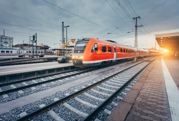 Wall Mural - modern high speed red commuter train at the railway station at colorful sunset. railroad with vintag