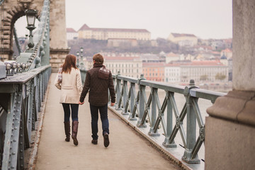 Canvas Print - Christmas in old town. Young cheerful caucasian couple in warm cozy clothes walking in city centre.