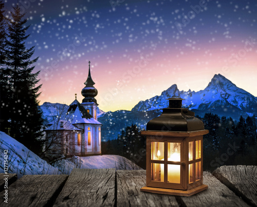Foto-Doppelrollo - Laterne auf einem Holztisch vor verschneiter Winterlandschaft mit Kirche bei Nacht (von Visions-AD)