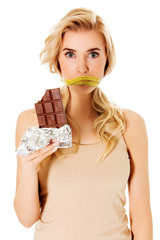 Woman with tied mouth holding bar of chocolate