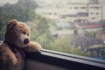 Teddy bear sitting beside the window while raining