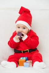 Seven months old baby girl in Santa Claus dress sitting on a whi