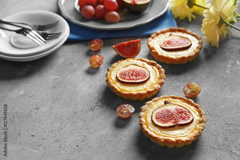 Tasty fig cakes with grapes and fresh flowers on grey background